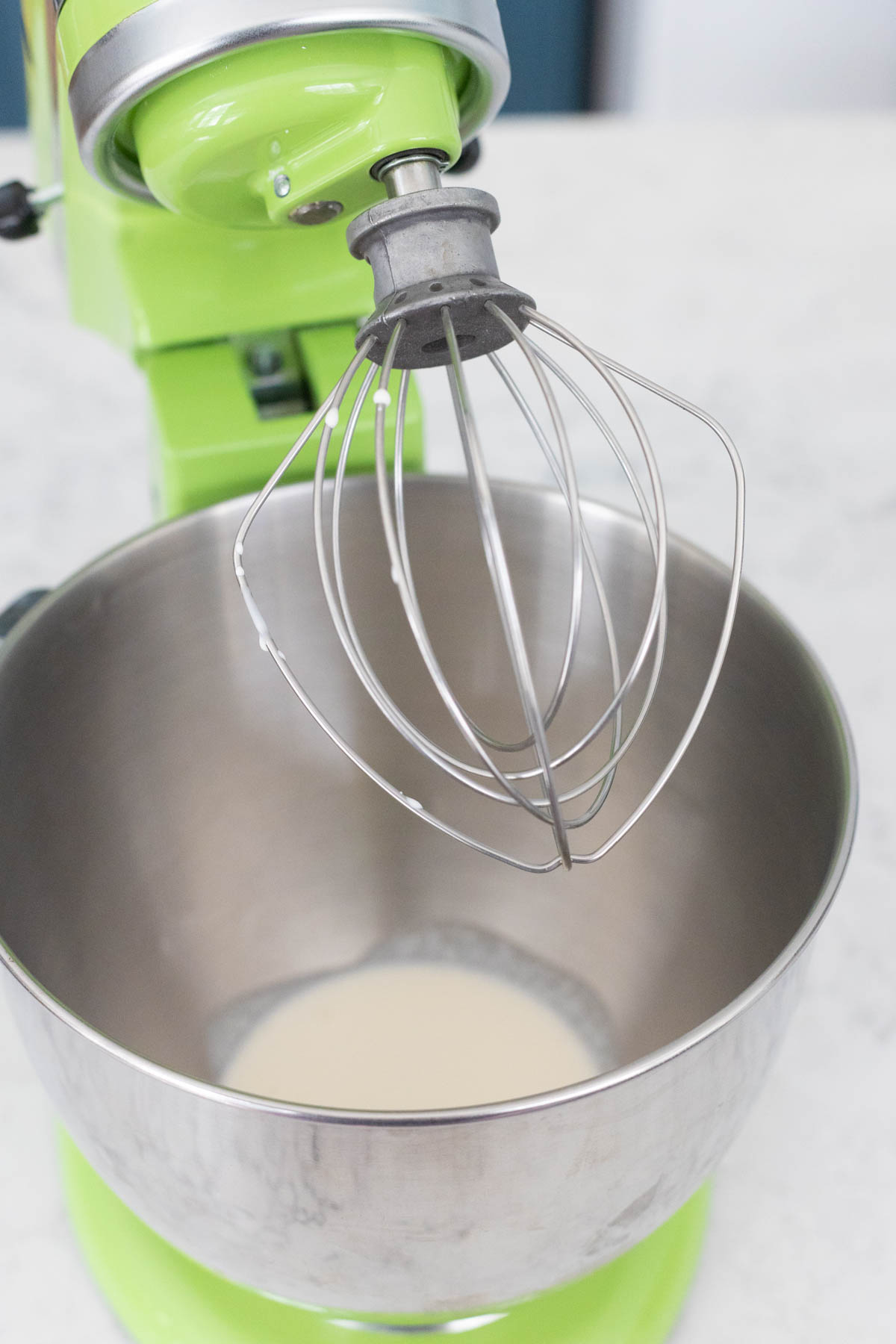 The cream has been poured into the bowl of a stand mixer fitted with the whisk attachment.