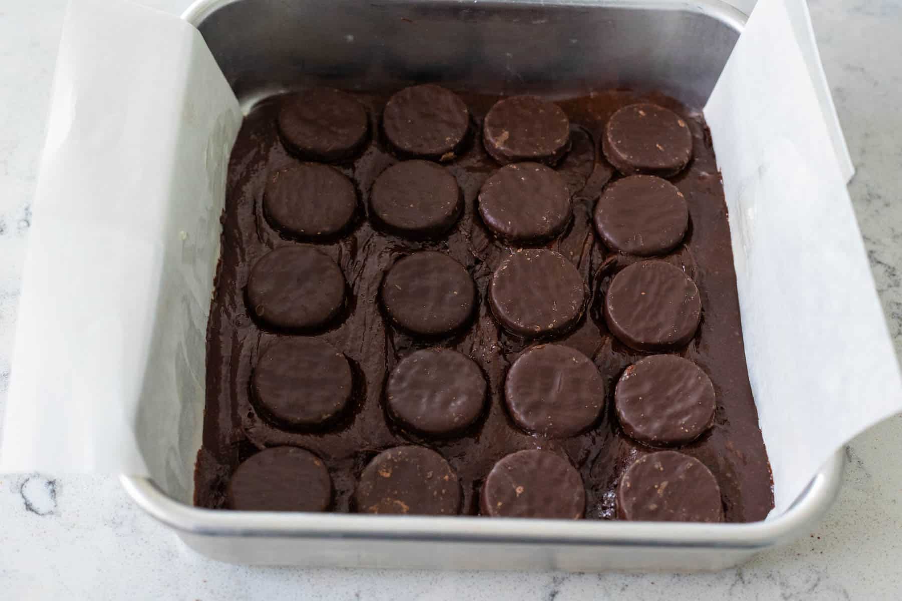 Half of of the brownie batter is on the bottom of the baking pan and the peppermint patties have been arranged in an even layer on top.