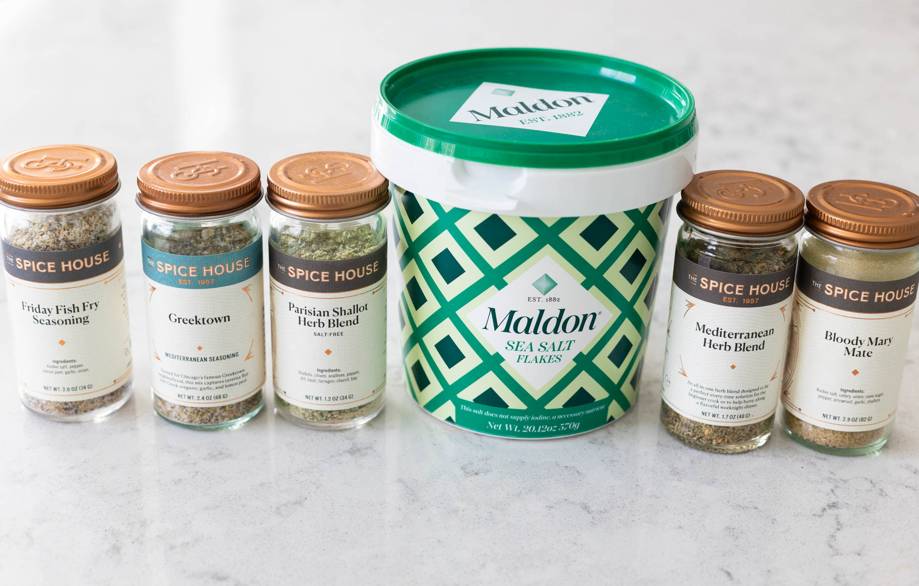 A line-up of spice blends in jars next to a tub of sea salt.