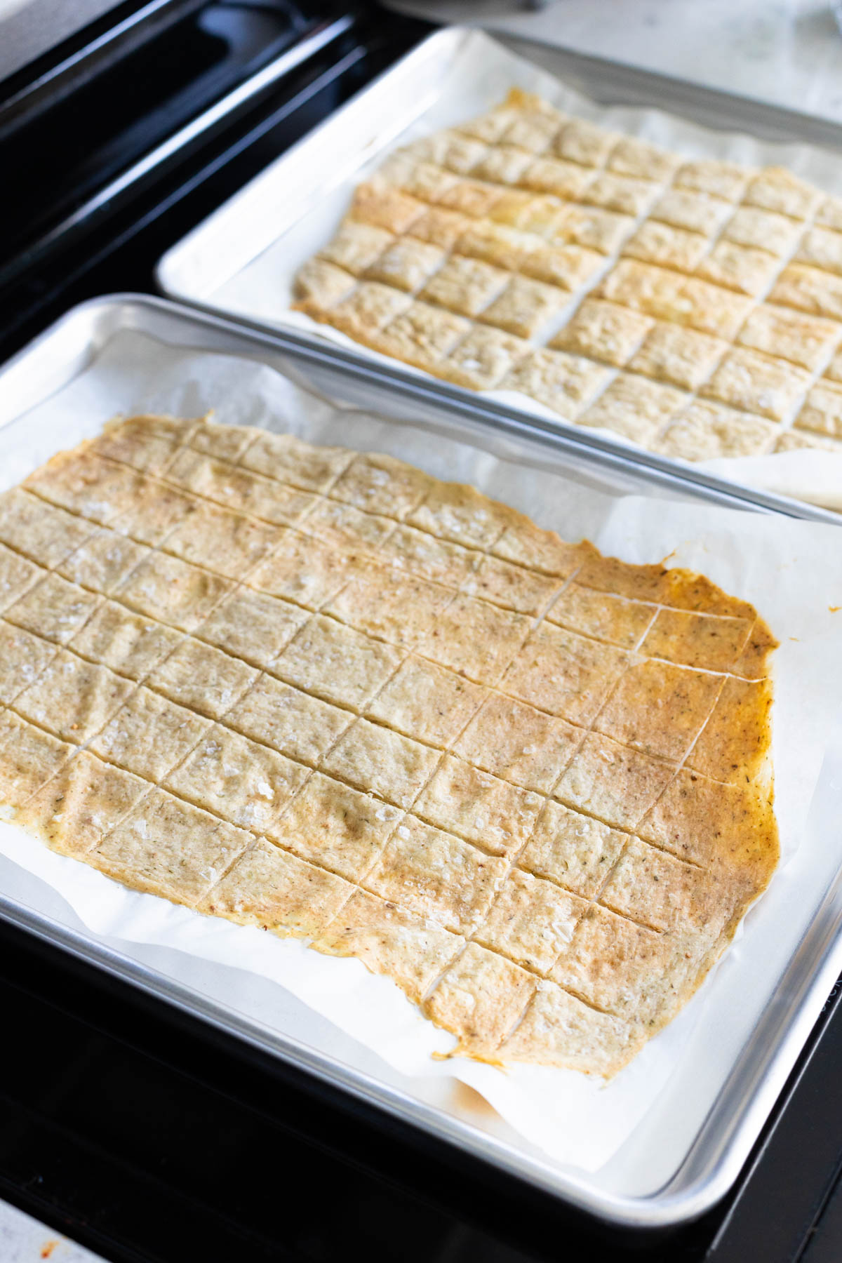 The baking pans of crackers have come out of the oven and are light brown. You can see the rows of scoring from the pizza wheel.