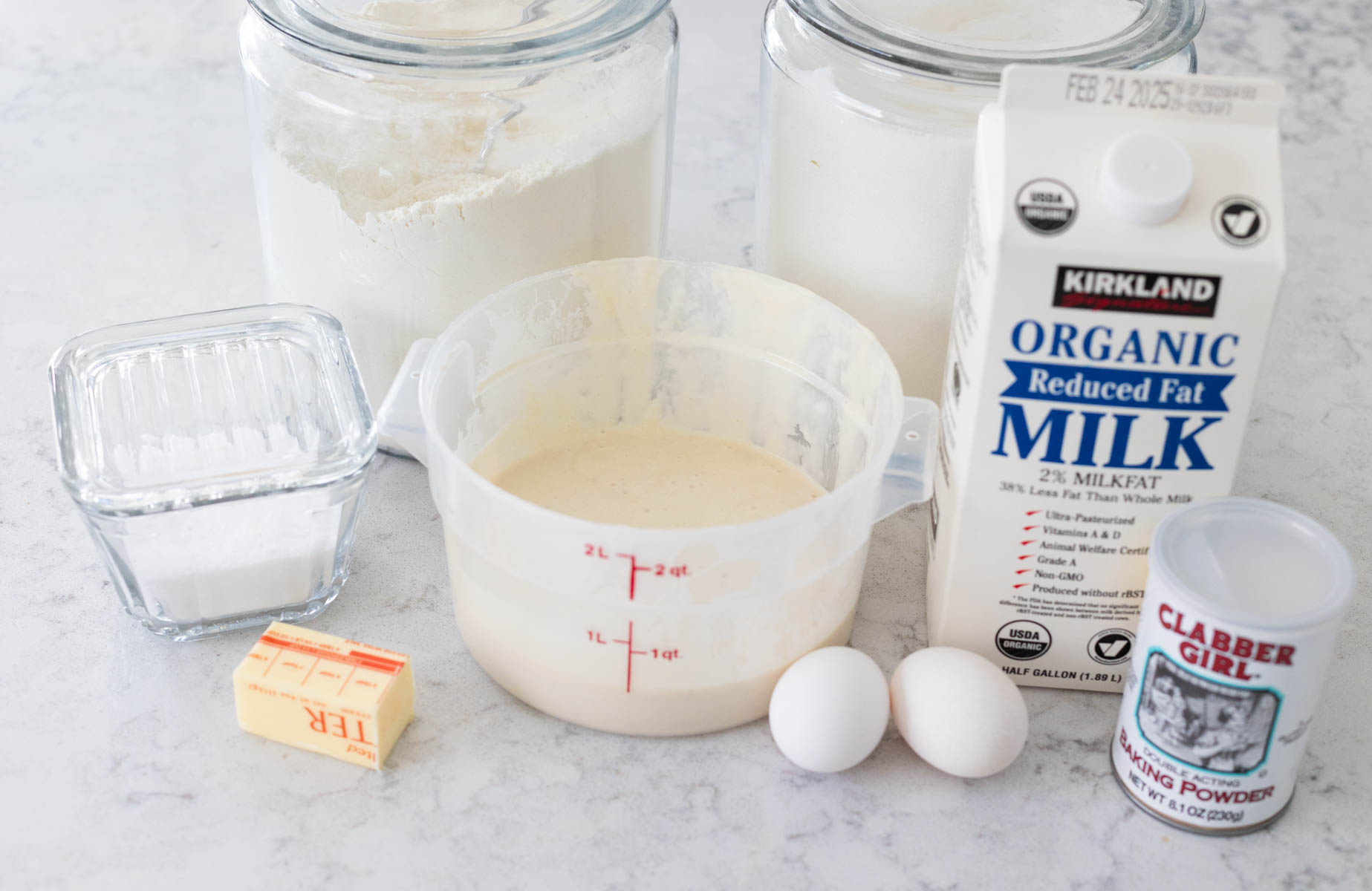 The bucket of sourdough starter discard is on the counter next to the rest of the ingredients needed to make the waffles.