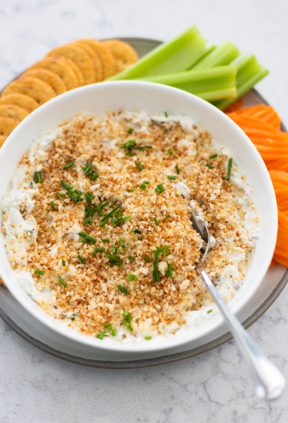 A big bowl of creamy pickle dip has toasted bread crumbs and chopped fresh chives sprinkled over the top.
