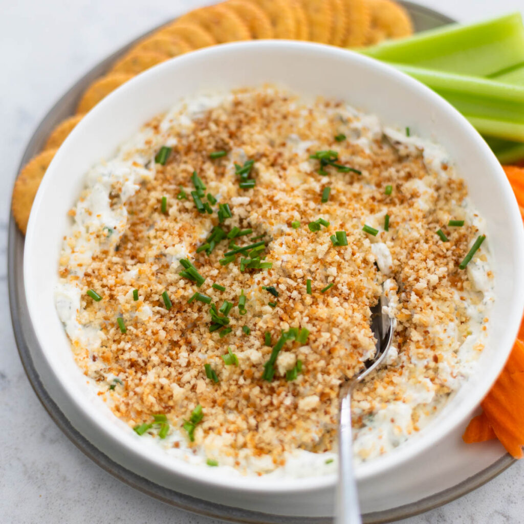A big bowl of creamy pickle dip has toasted bread crumbs and chopped fresh chives sprinkled over the top.