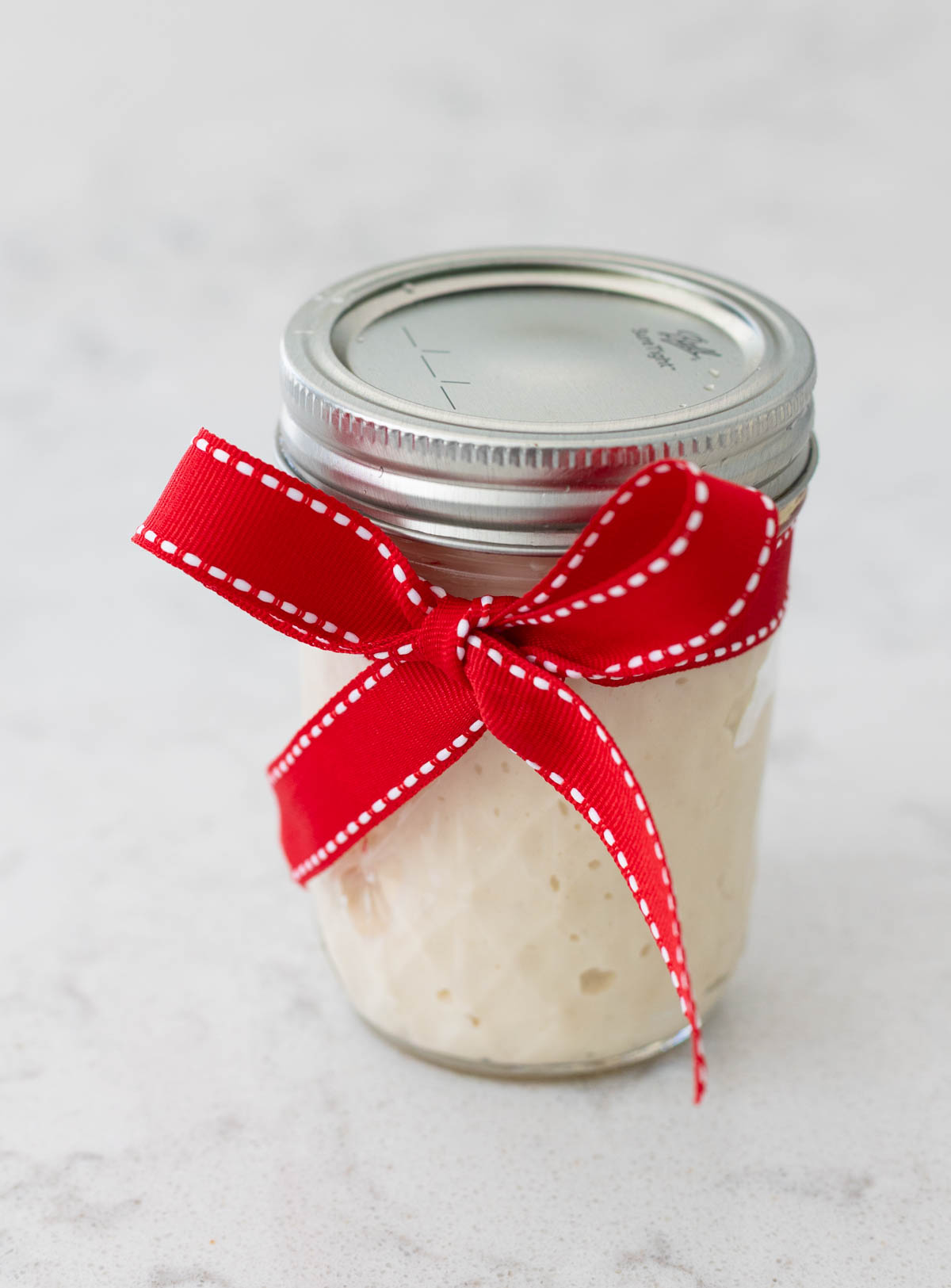 A mason jar filled with sourdough starter has been wrapped with a red bow.