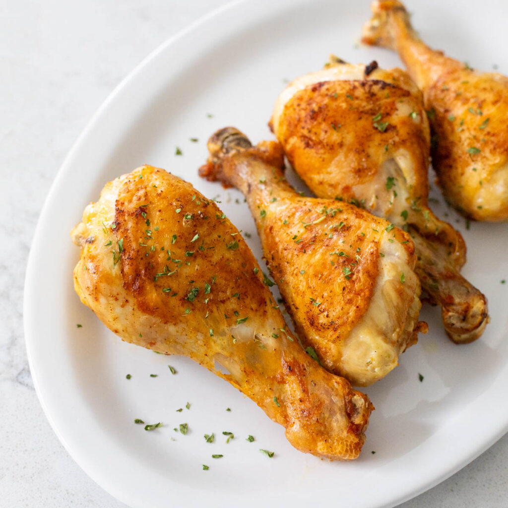 A white platter of golden brown baked chicken legs.