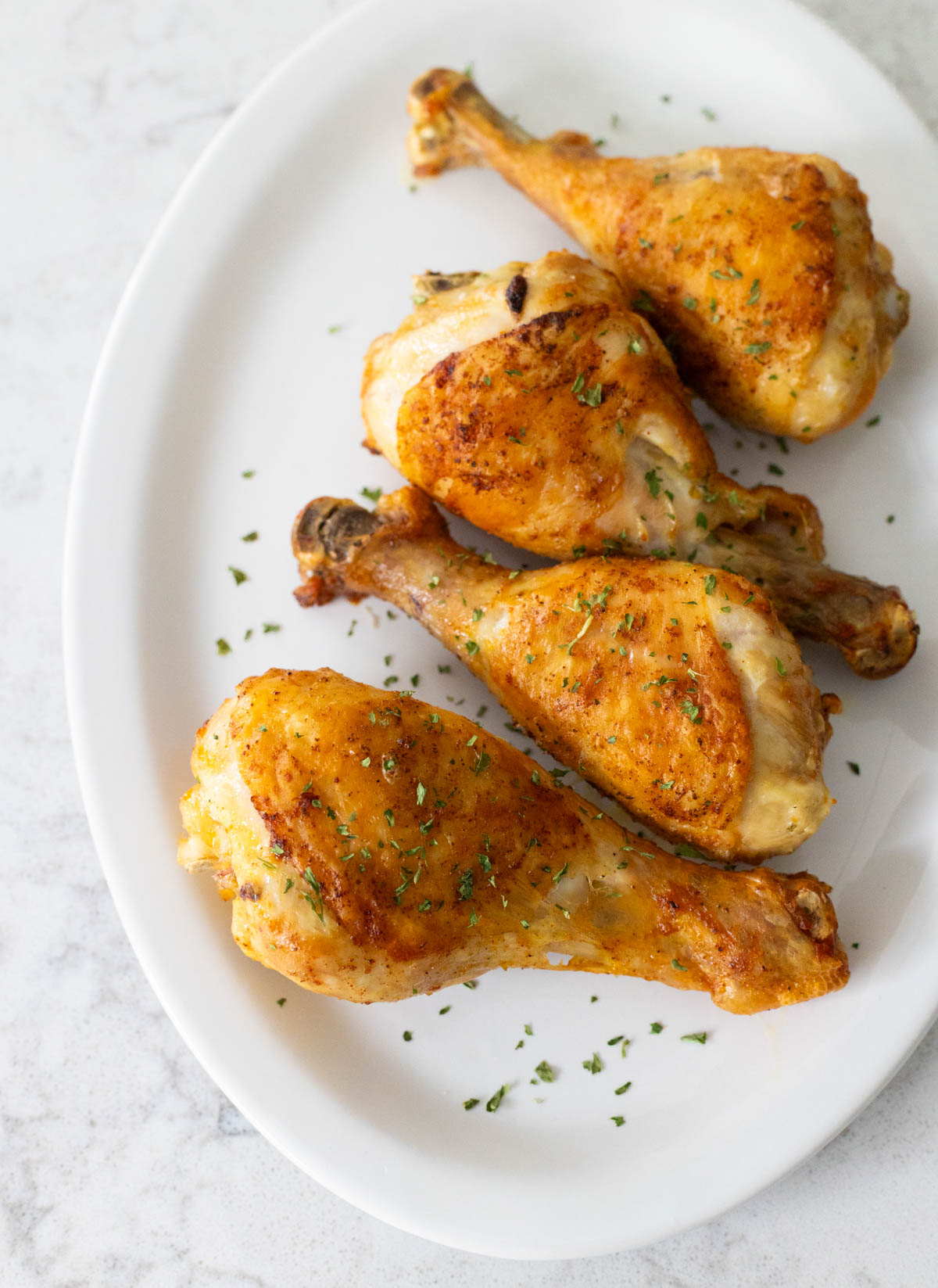 A white platter of golden brown baked chicken legs.
