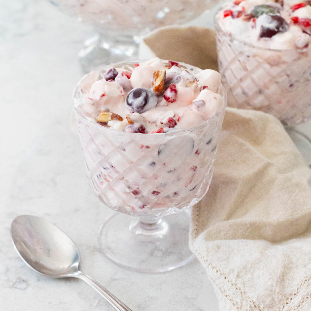A parfait cup of creamy cranberry fluff has a spoon resting on the side.