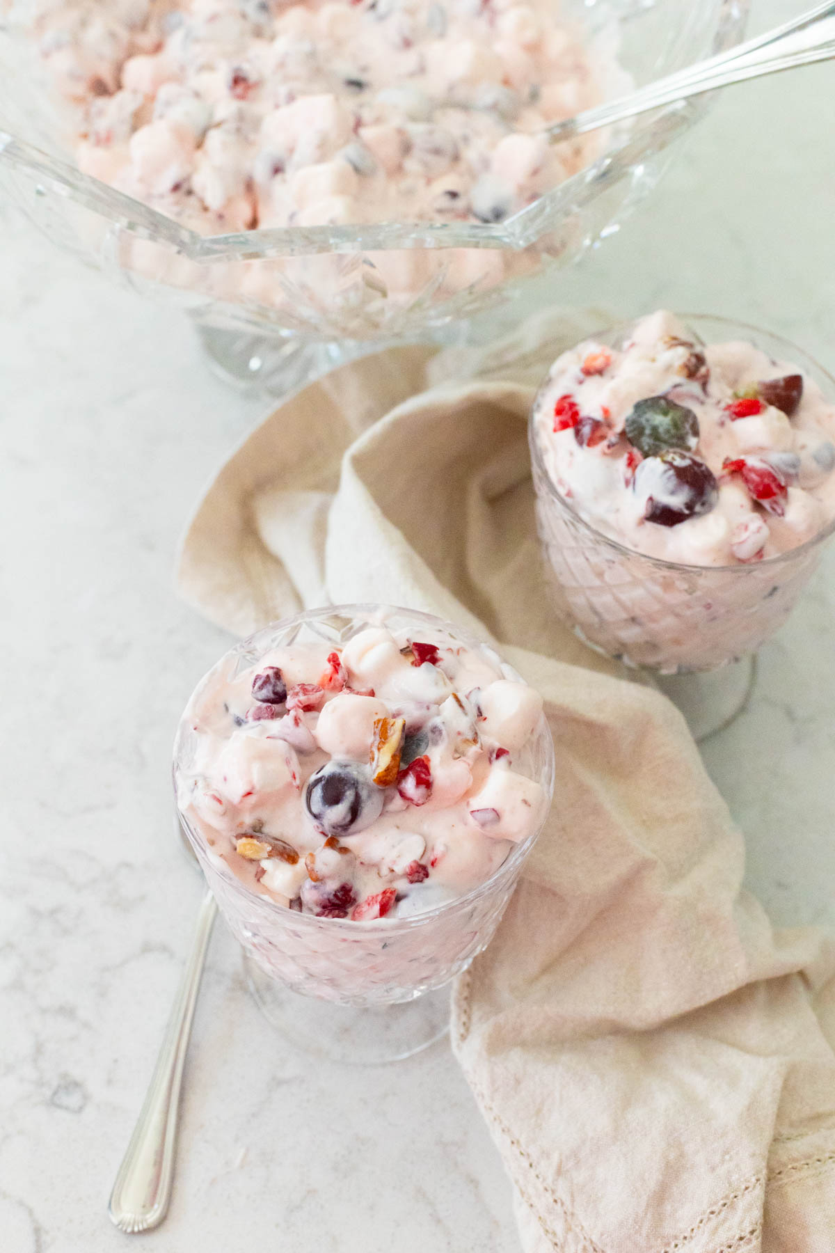 A set of parfait cups of creamy cranberry fluff have a spoon resting on the side.