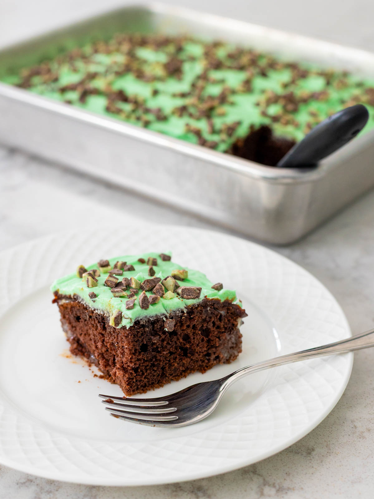 The slice of grasshopper cake on a plate sits in front of the 9x13-inch pan it was baked in.