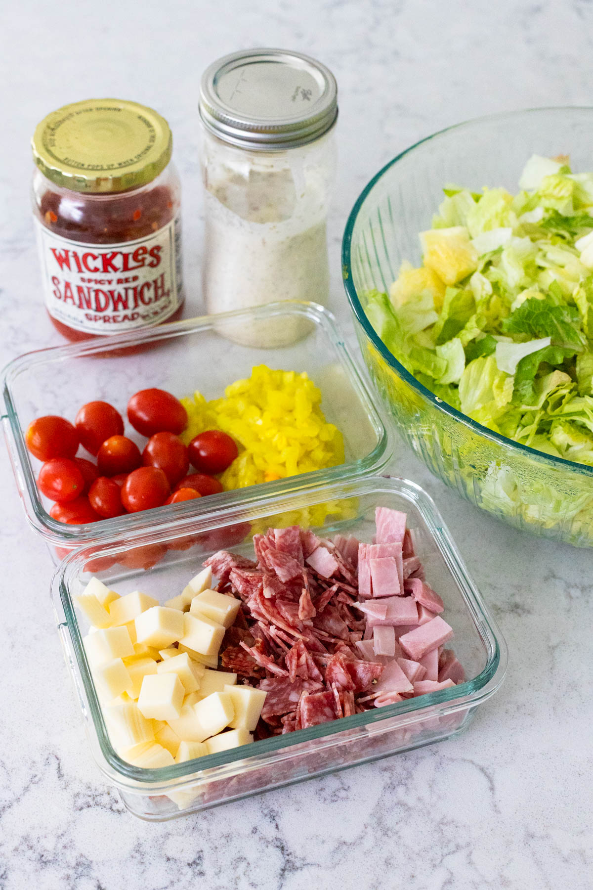 The toppings are arranged in fridge containers and set next to a big bowl of lettuce.