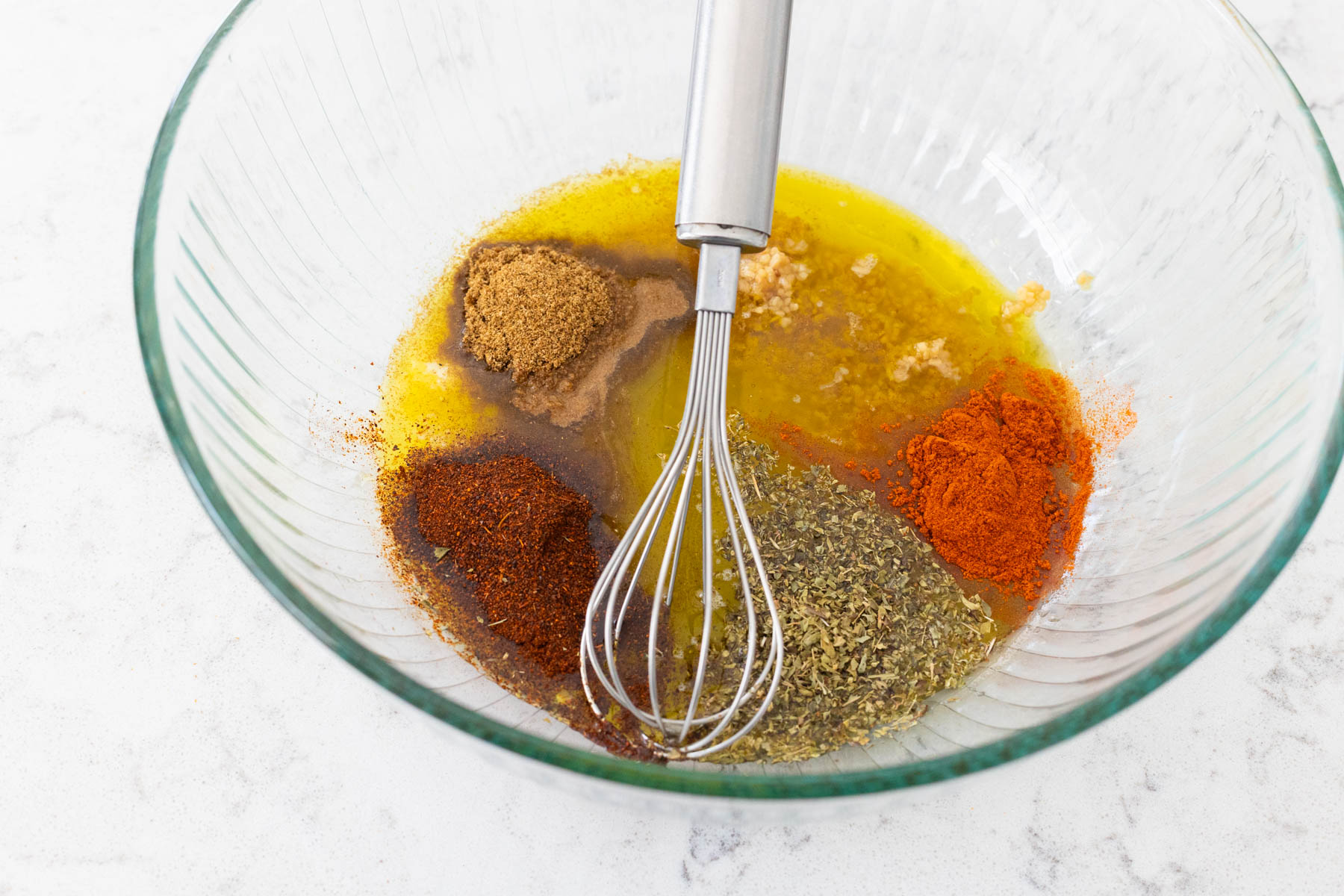 The spices and juices are in a large mixing bowl with a whisk.