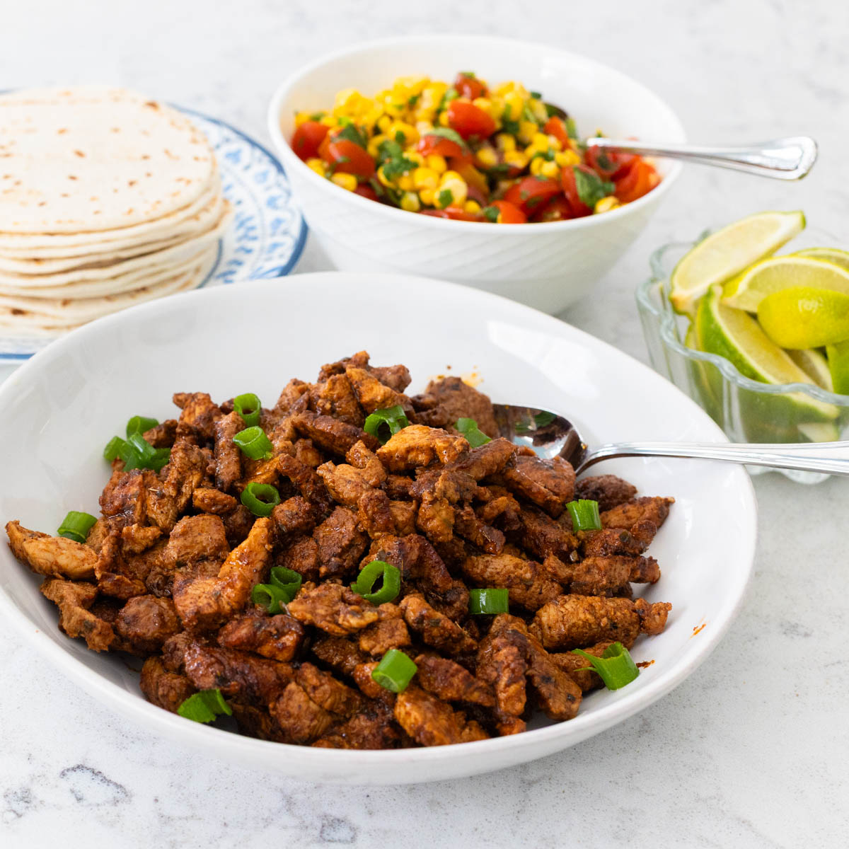 A bowl of pork tenderloin taco meat is in front of a bowl of the chunky corn salsa.