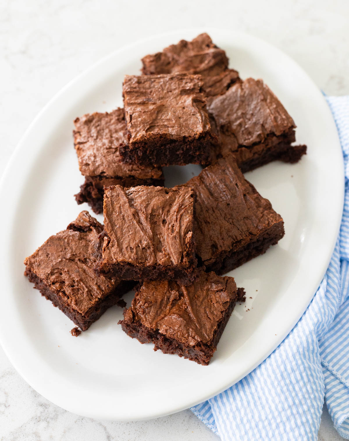 A white platter has rich chocolate brownies piled high.