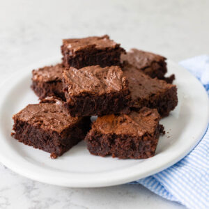 A white platter has rich chocolate brownies piled high.
