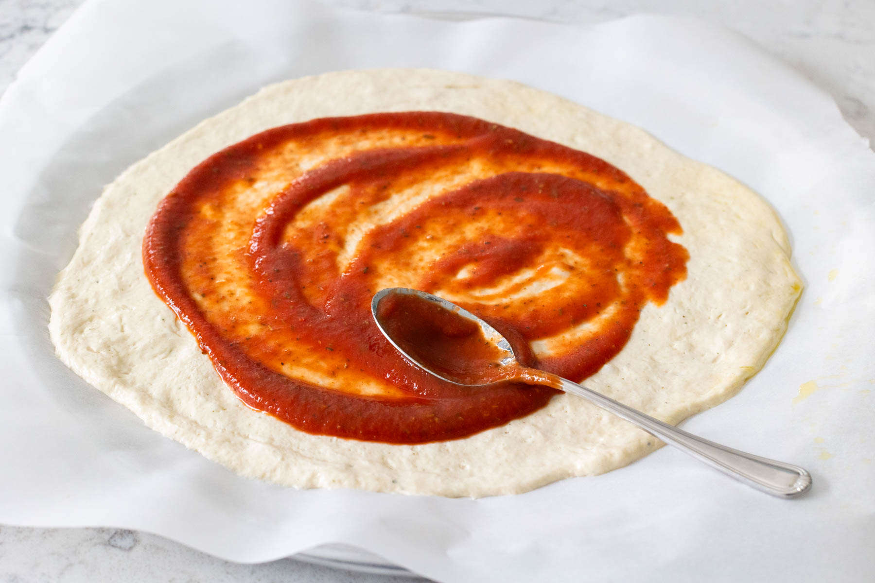 The dough has been rolled out and topped with tomato sauce.