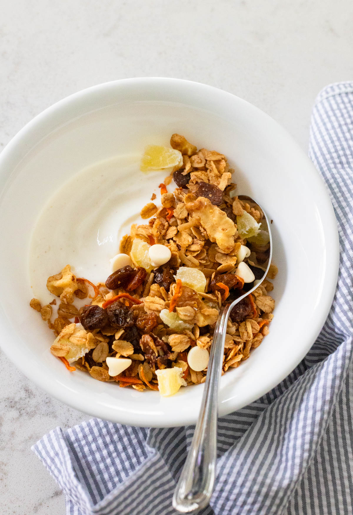 A white bowl with vanilla yogurt has been topped with carrot cake granola.