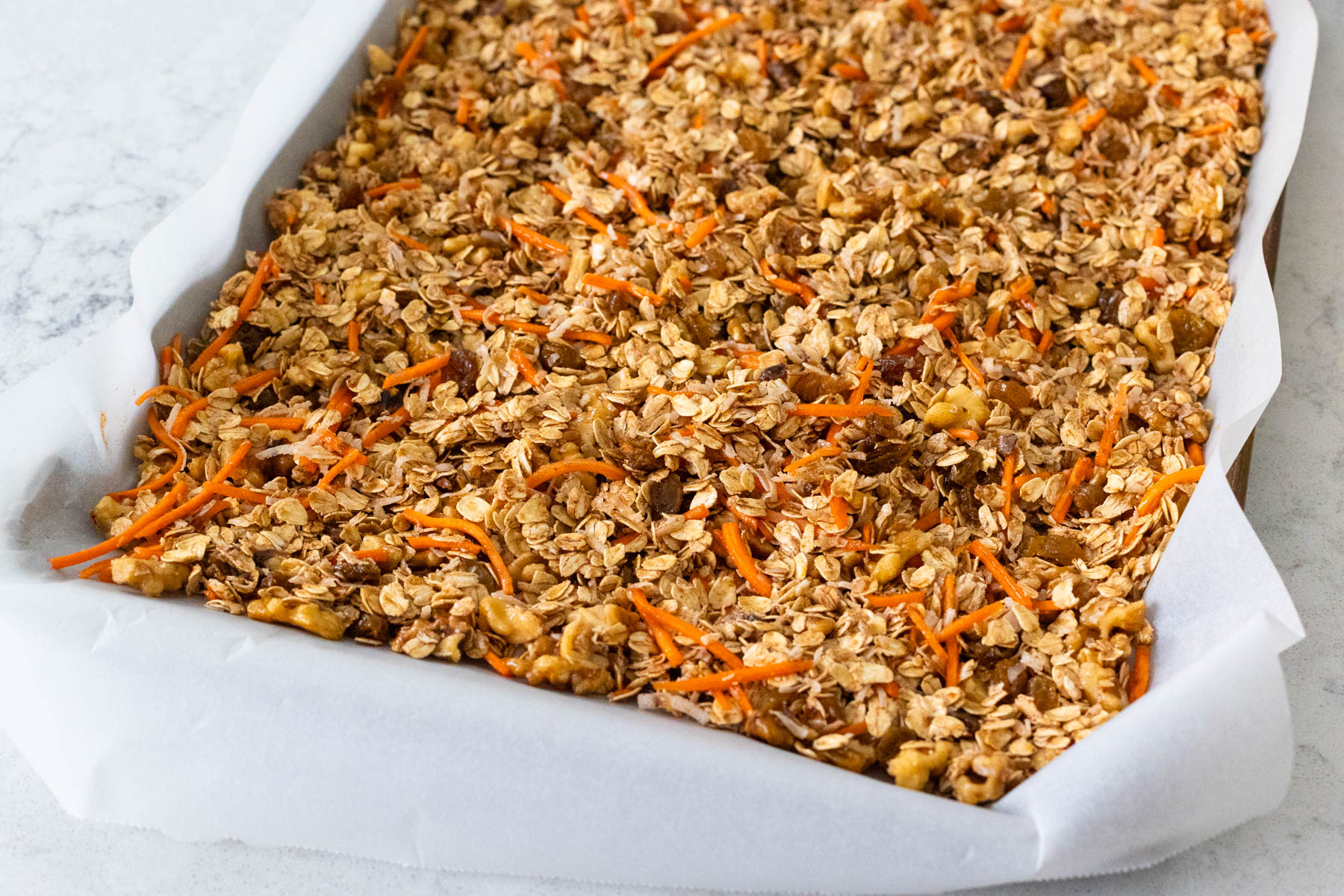 The granola has been spread onto a baking sheet lined with parchment paper.