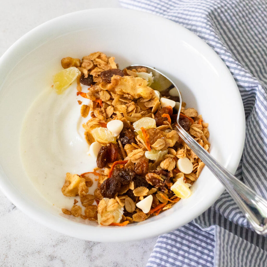 A white bowl with vanilla yogurt has been topped with carrot cake granola.