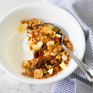 A white bowl with vanilla yogurt has been topped with carrot cake granola.