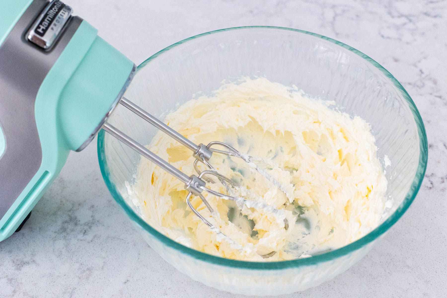 The cream cheese is in a large mixing bowl being whipped by a hand mixer.