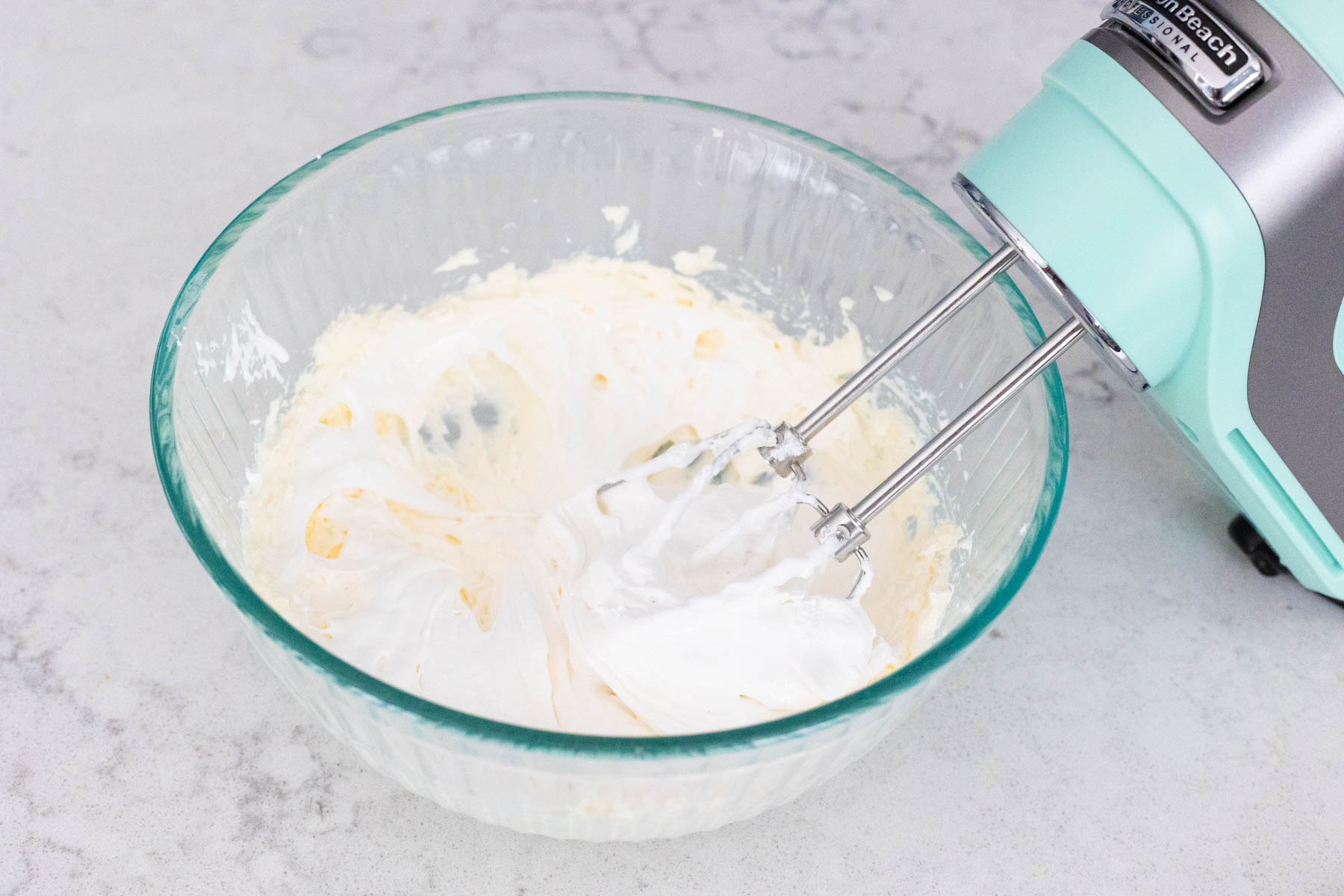 The marshmallow fluff has been added to the mixing bowl and is being beaten in with the mixer.