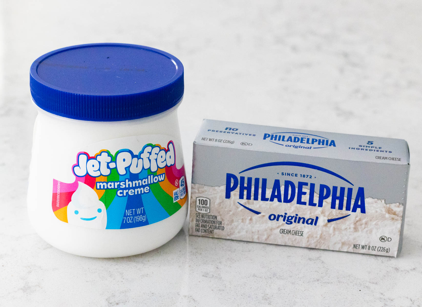A brick of cream cheese and a jar of marshmallow fluff sit on the counter.