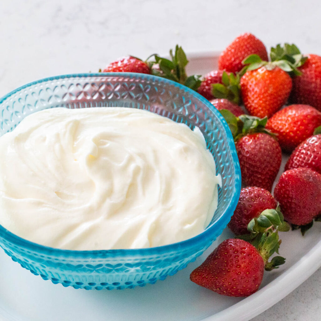 A blue bowl is filled with a 2-ingredient fruit dip on a platter of fresh strawberries.