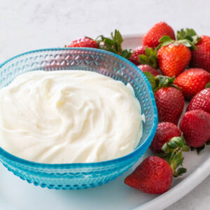 A blue bowl is filled with a 2-ingredient fruit dip on a platter of fresh strawberries.