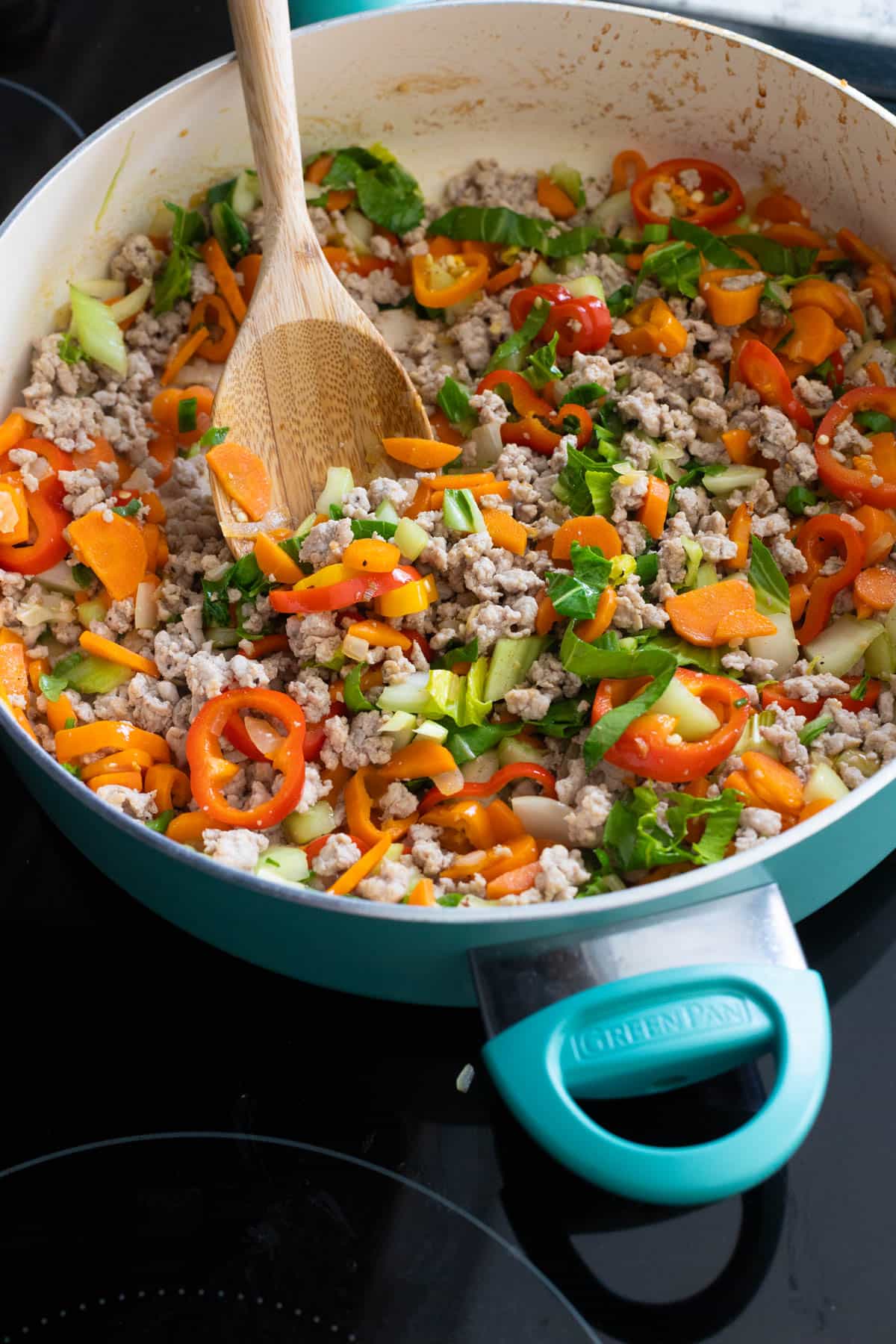 The blue skillet is filled with the pork stir fry with chopped carrots, peppers, and cabbage peeking out from the mix.