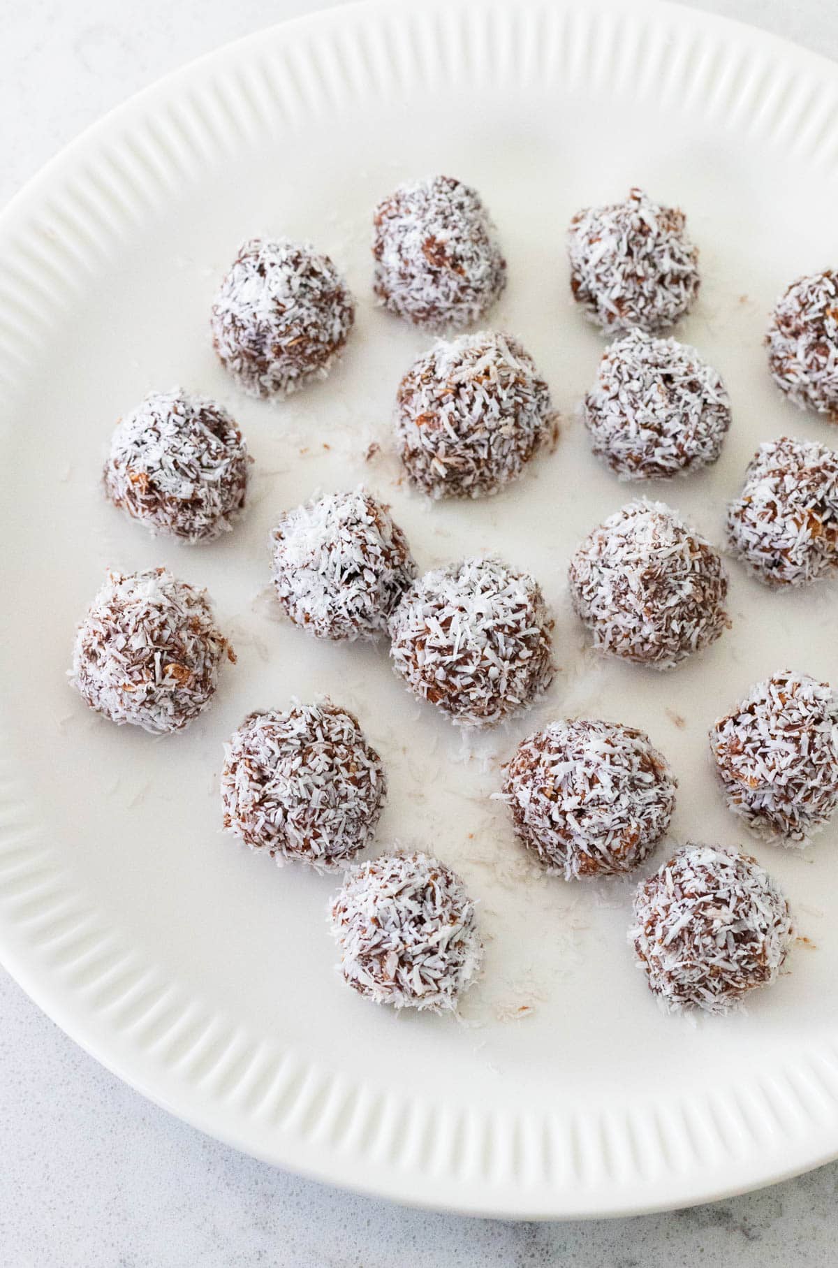 The finished chocolate balls are on a white plate ready to be chilled in the fridge.