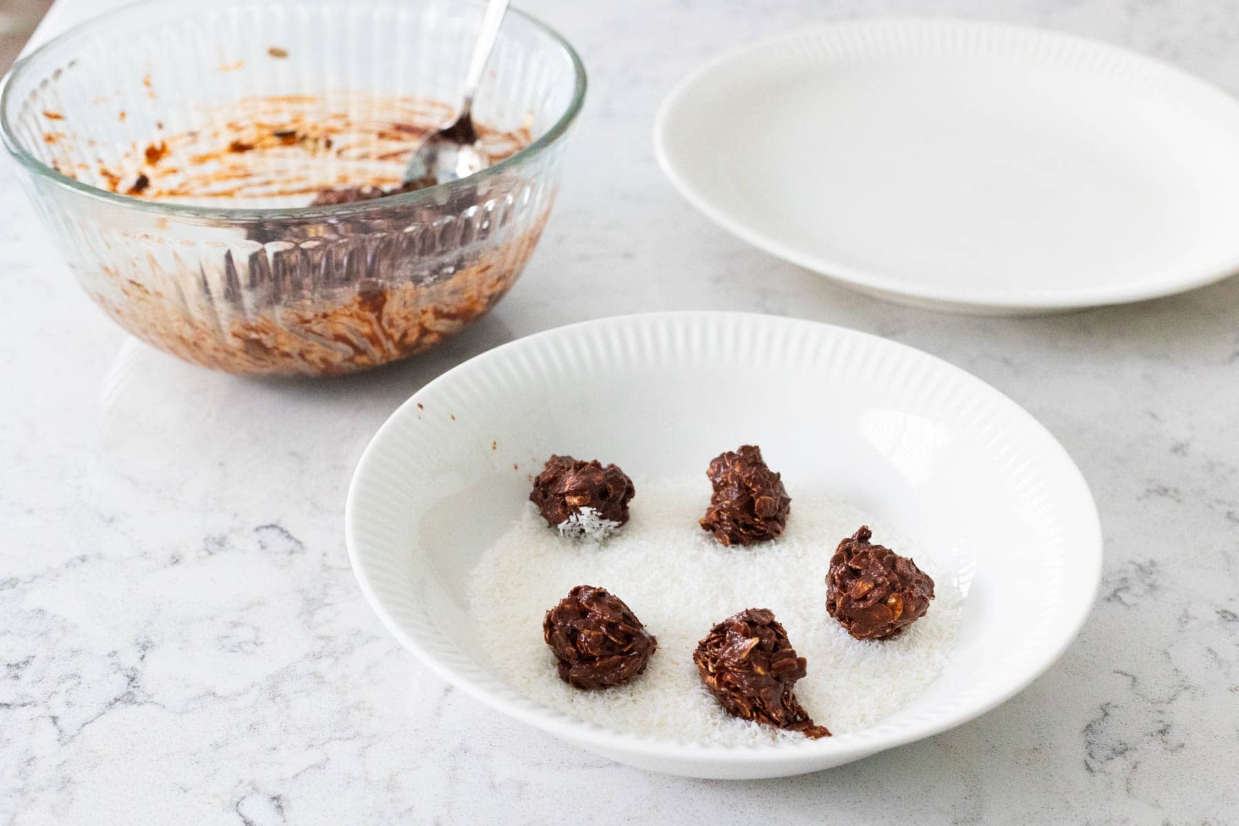 The chocolate cookie balls are being rolled in a bowl of coconut.