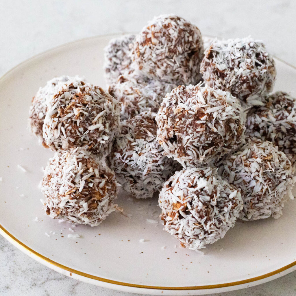 A small plate has a pile of coconut-rolled Swedish chocolate balls.