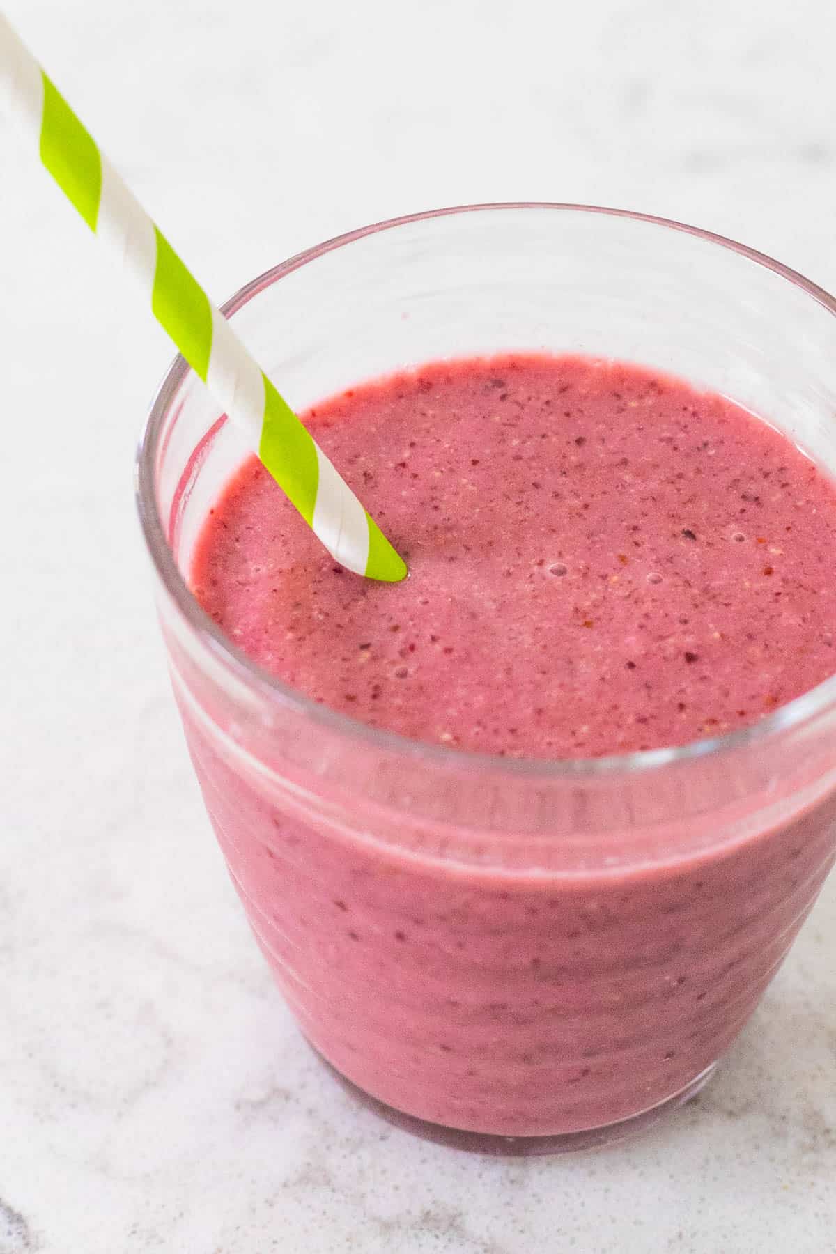A red smoothie in a cup with a striped straw.