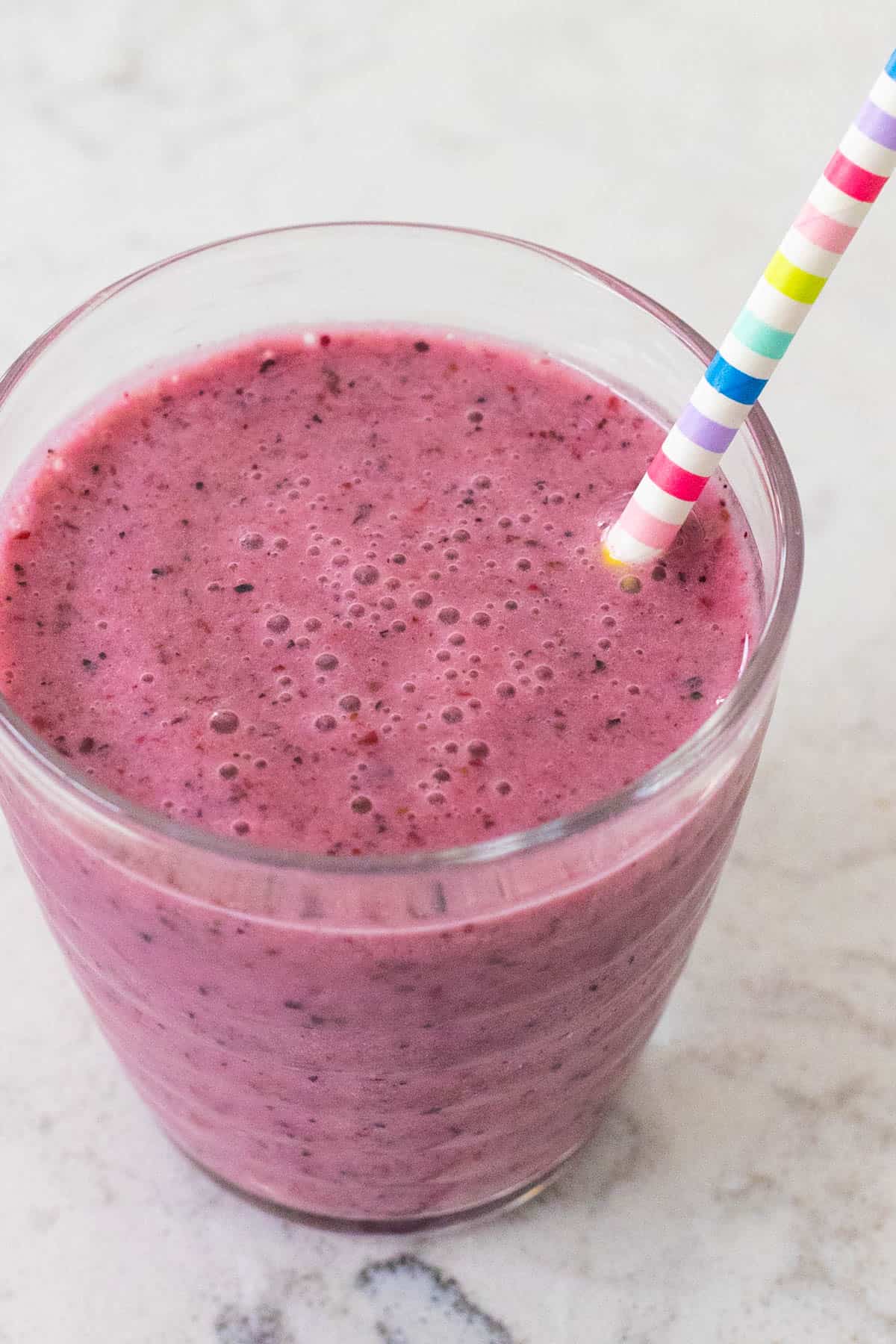 A deep purple grape smoothie in a cup with a straw.