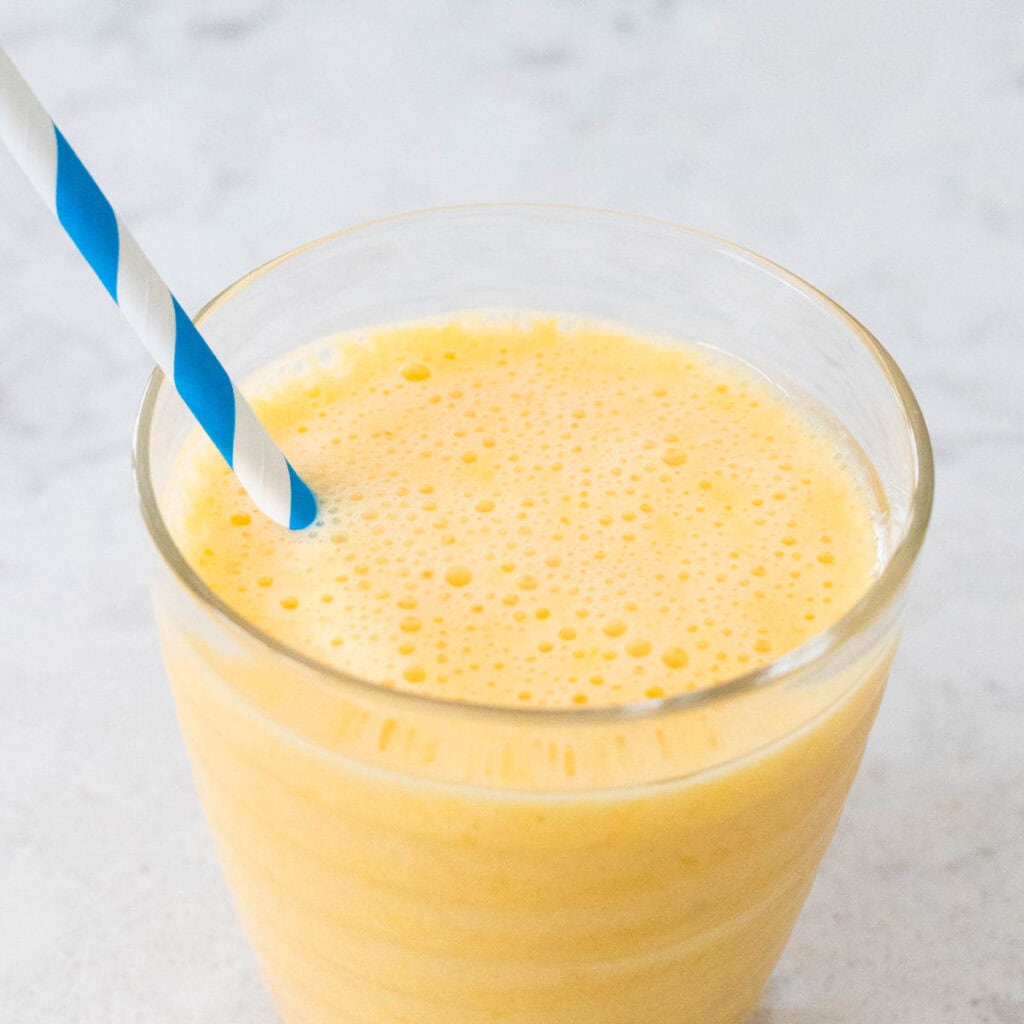 A creamy orange smoothie with a striped straw.