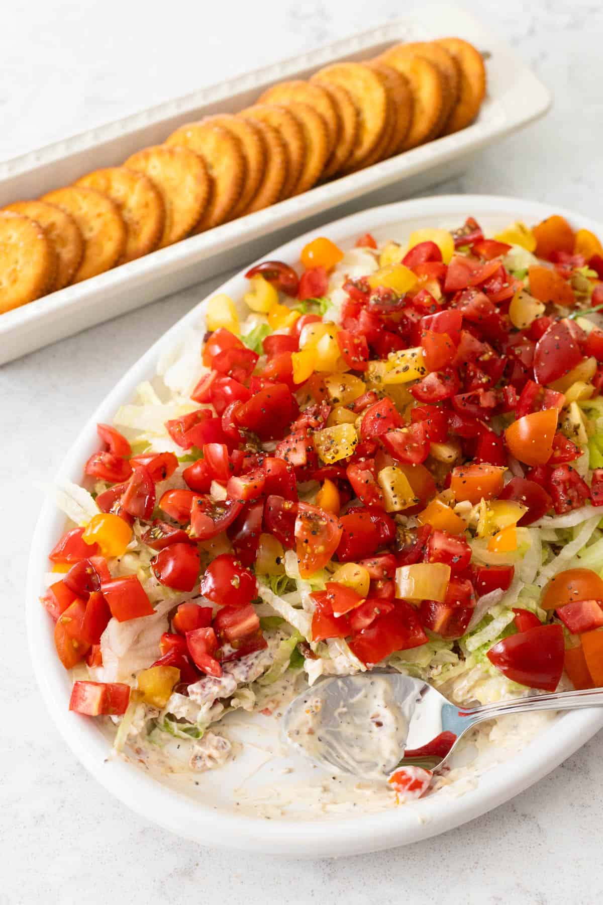 The platter of dip has fresh tomatoes and shredded lettuce sprinkled over the top.
