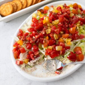 The BLT dip is on a white platter with fresh tomatoes on top and crackers on the side.
