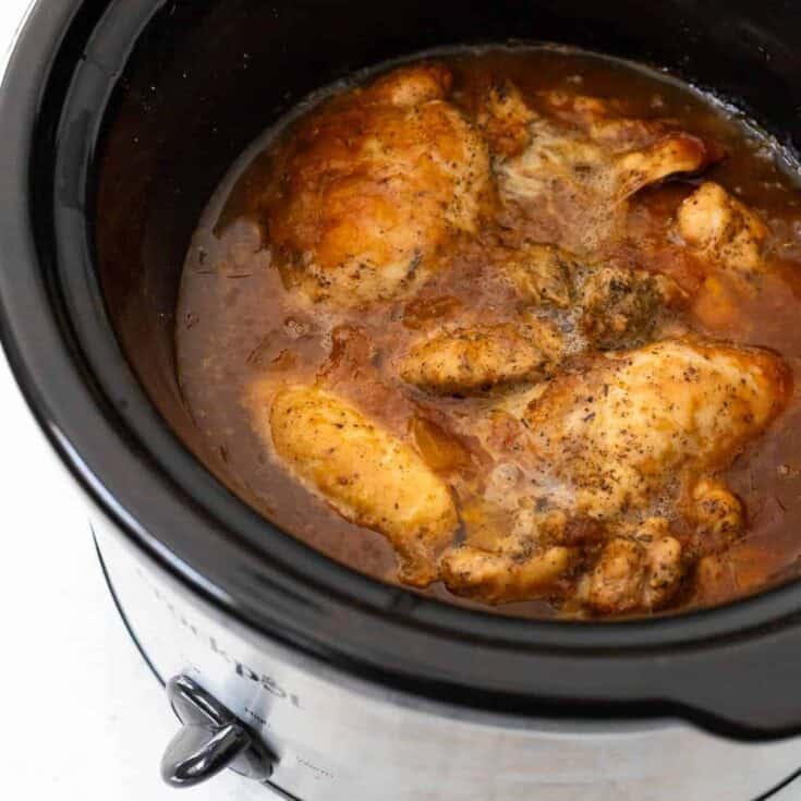 A crockpot filled with cooked chicken in a BBQ peach sauce.