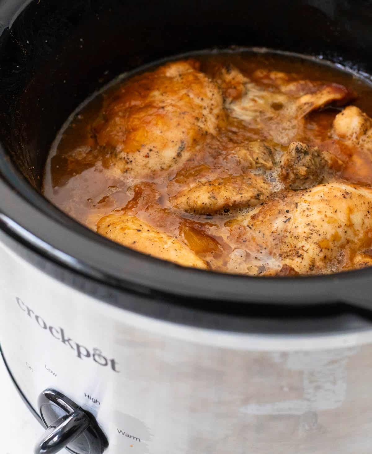A crockpot filled with cooked chicken in a BBQ peach sauce.