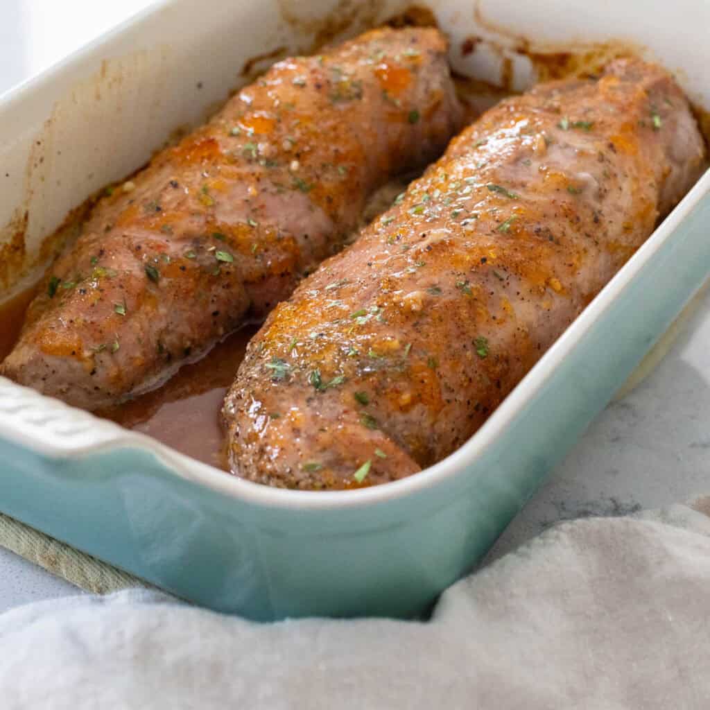 Two pork tenderloins are nestled in a blue baking dish and coated in a bourbon peach glaze.