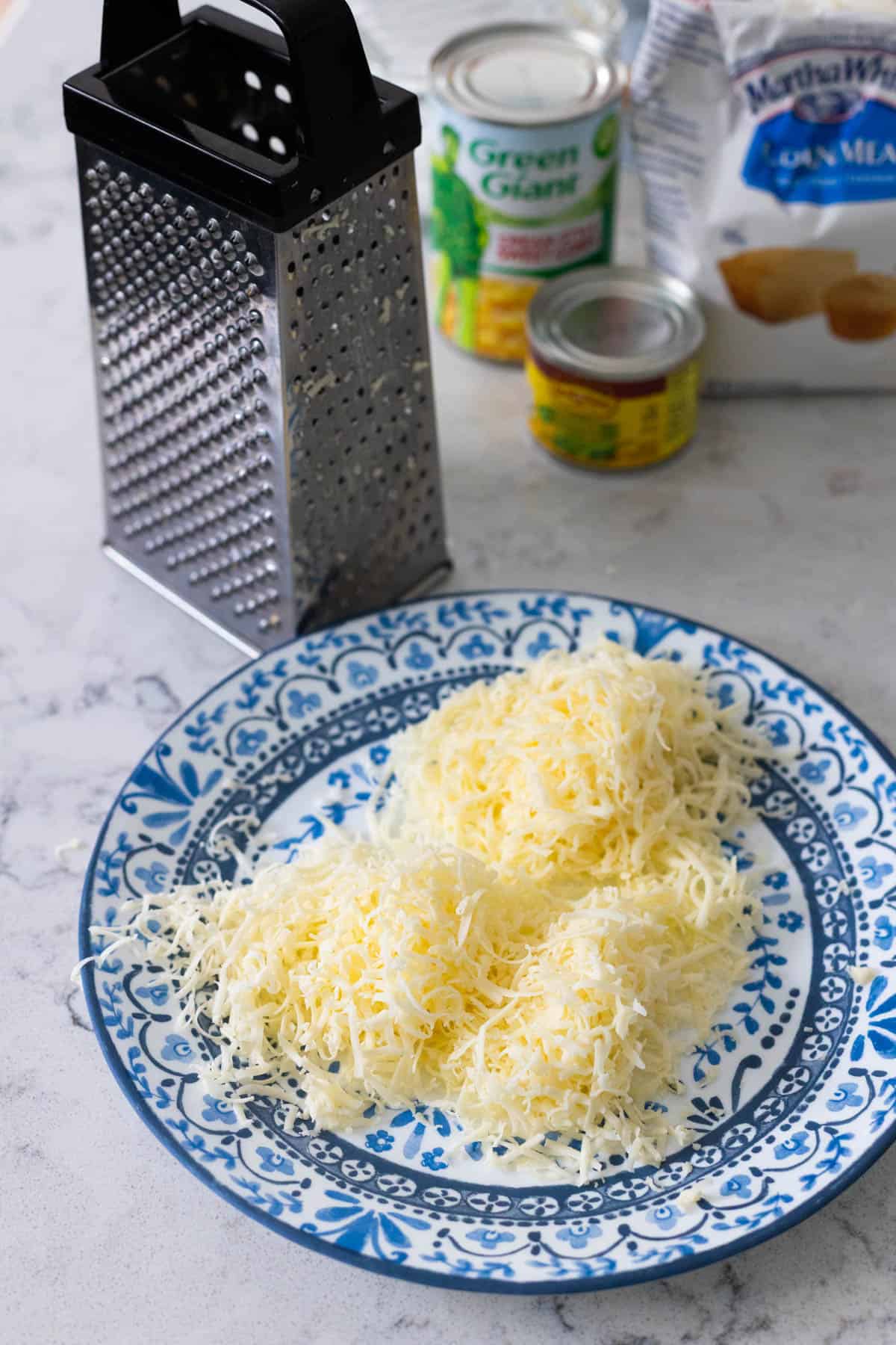 Freshly shredded cheese is on a blue plate next to the cheese grater.
