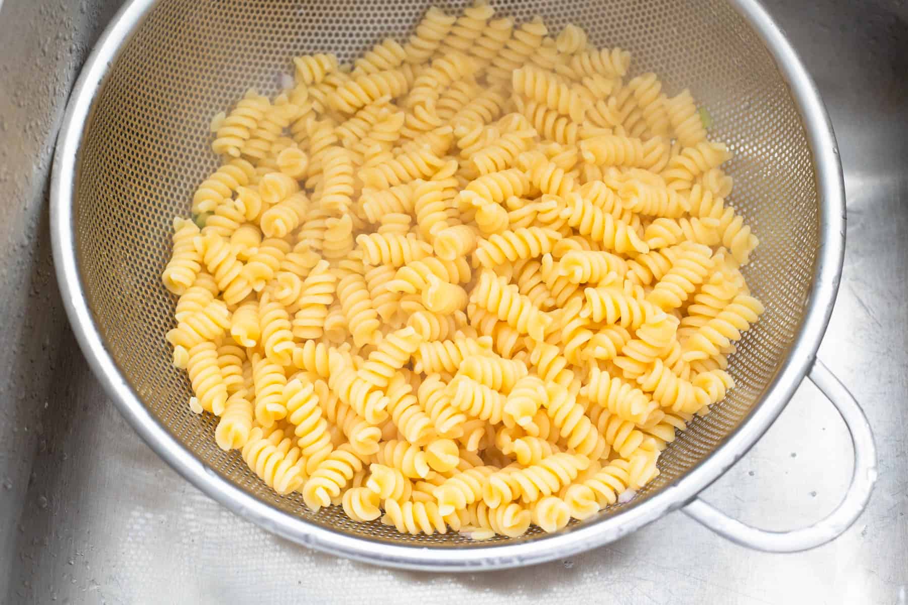 The colander is filled with rotini pasta and is resting in the sink.