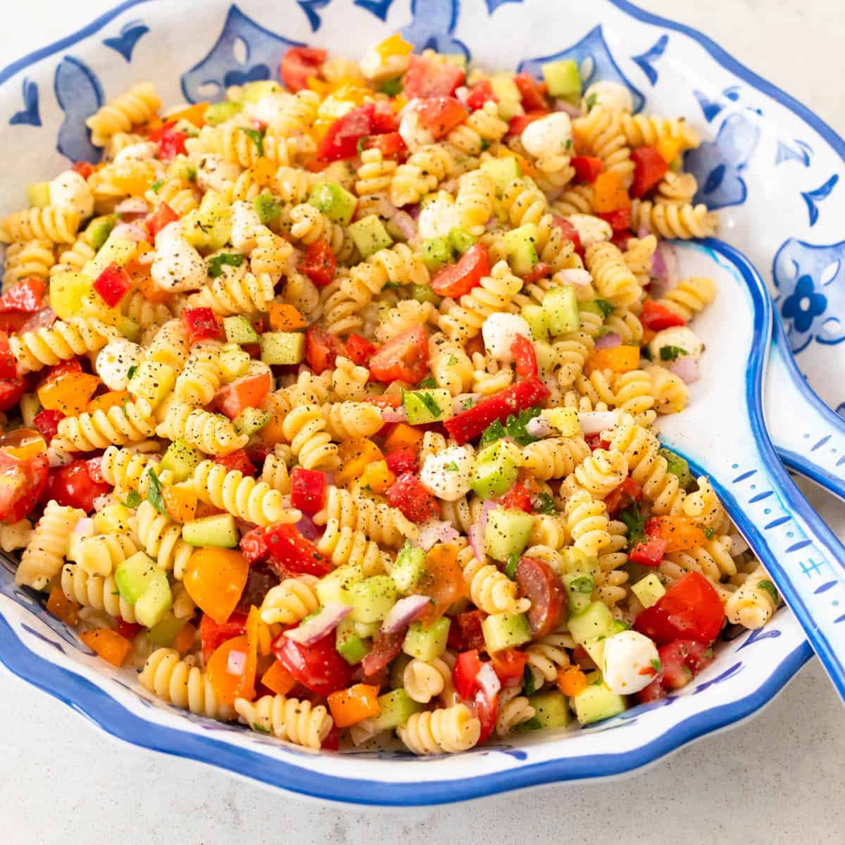 A large blue and white bowl has a pasta salad made with rotini noodles and fresh vegetables.