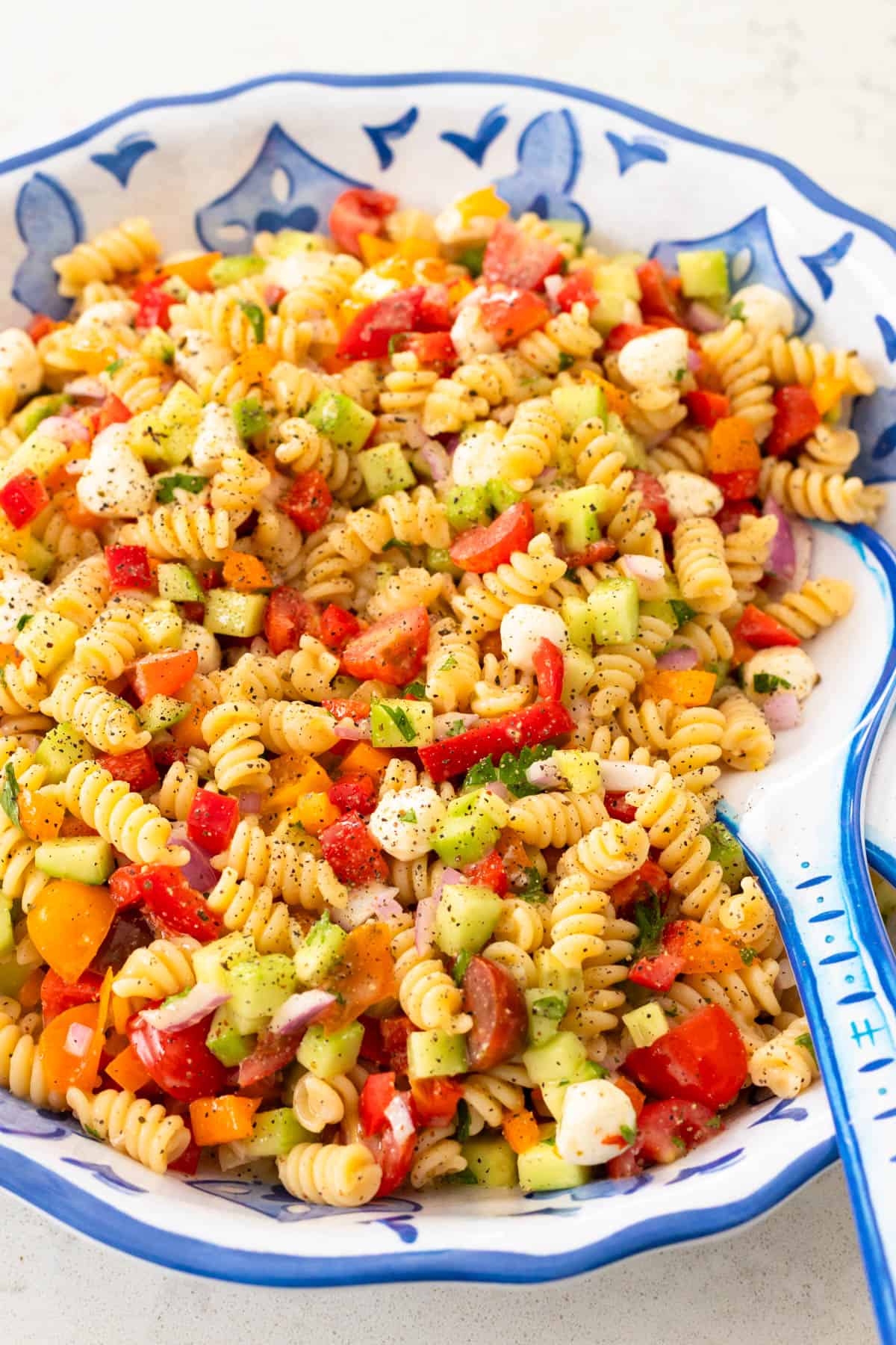 A large blue and white bowl has a pasta salad made with rotini noodles and fresh vegetables.