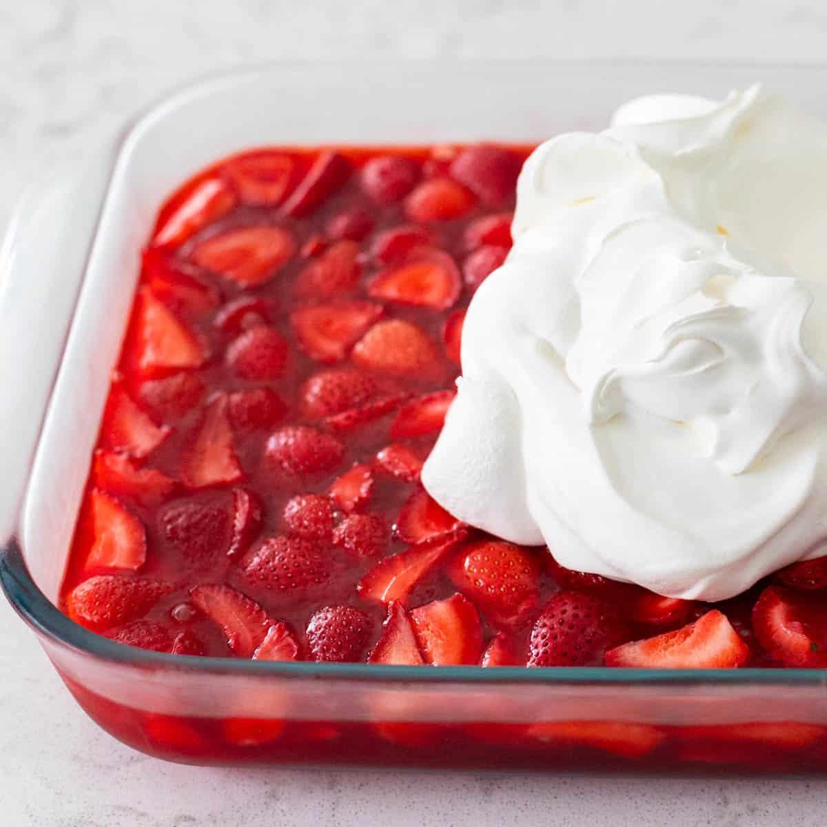 Le plat de Jello a terminé de prendre et a une grande cuillerée de Cool Whip sur le dessus prête à être étalée dans le plat.