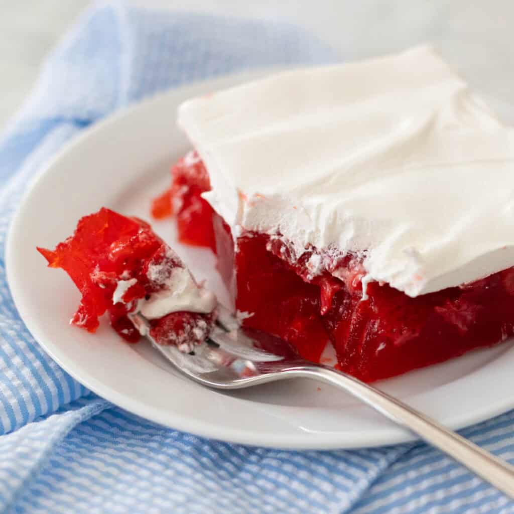 A square of strawberry jello salad is topped with whipped topping.