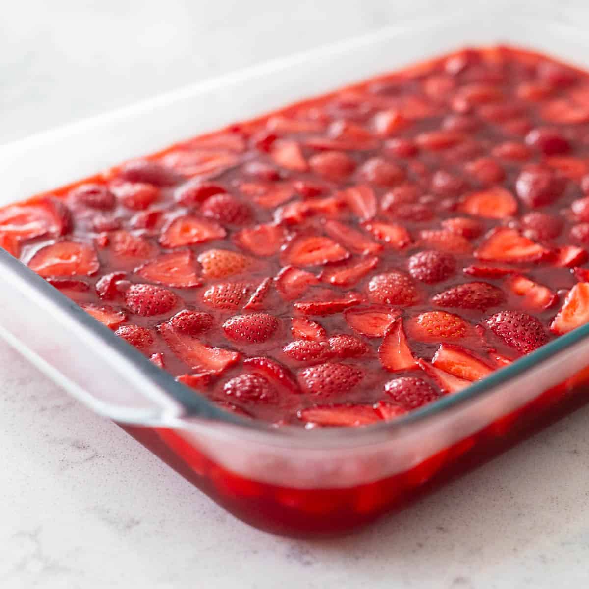 Les fraises et le Jello ont été versés dans le plat et sont prêts à refroidir au réfrigérateur.