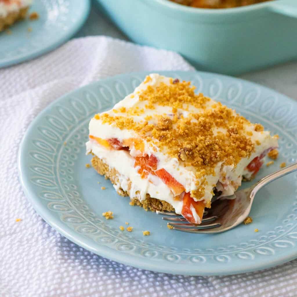 The creamy layered peach dessert with graham cracker crust is on a blue plate with a fork.