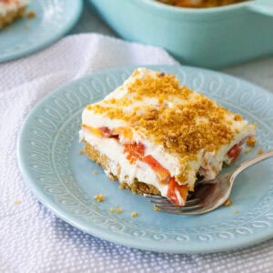 The creamy layered peach dessert with graham cracker crust is on a blue plate with a fork.