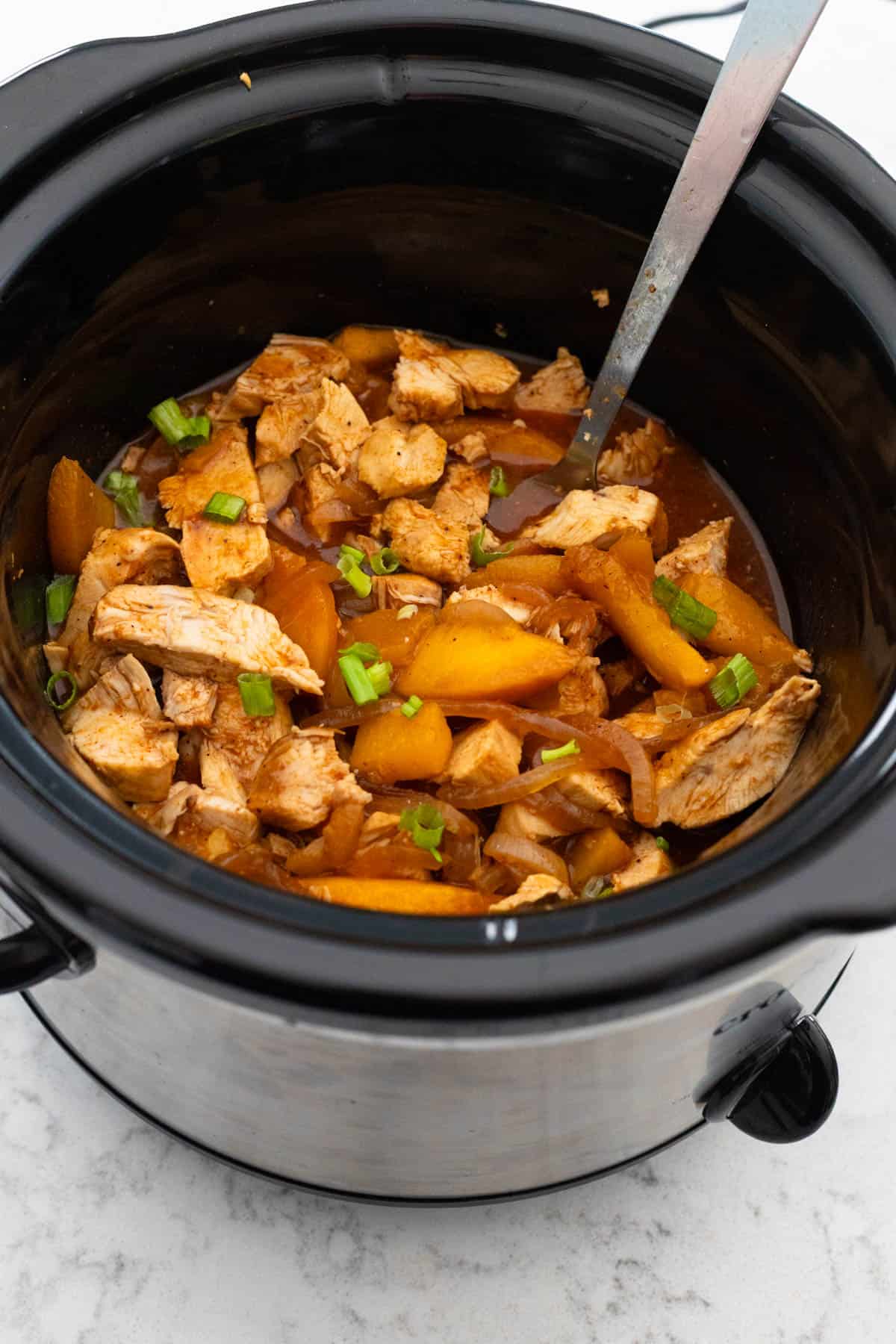The cooked chicken and peaches are in the bowl of the Crockpot.